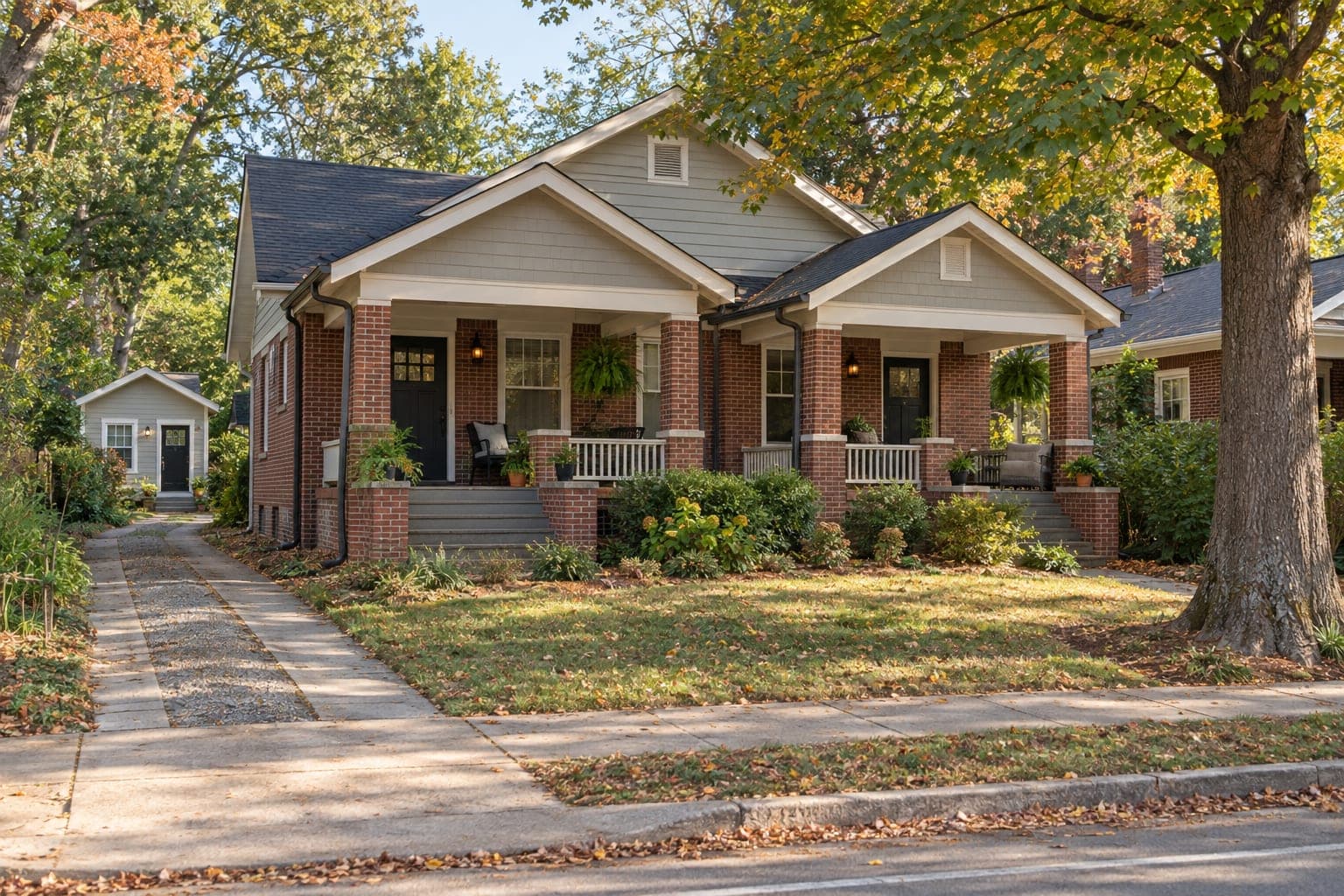 A brick duplex with two porches and a backyard cottage in a tree-lined Durham neighborhood