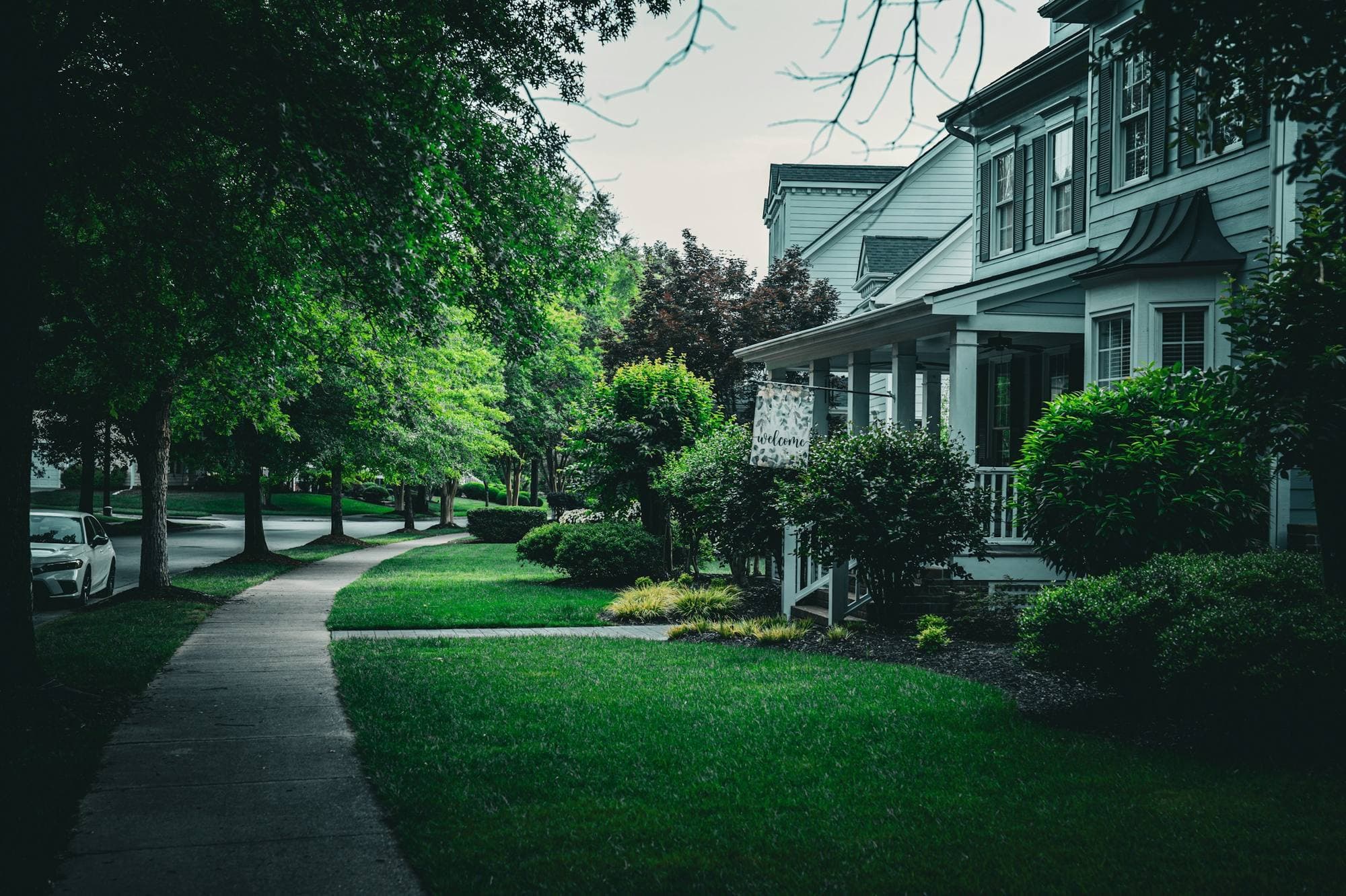 A house with a front porch and a welcome flag on a tree-lined sidewalk